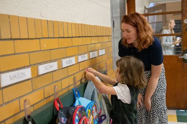 PreK student hanging up backpack with teacher